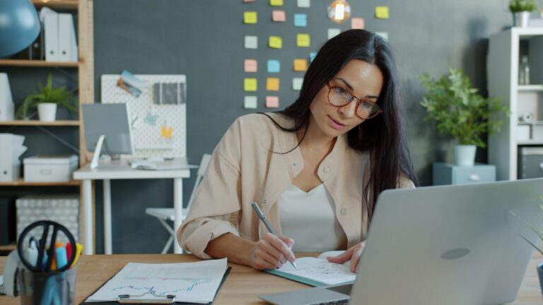 Woman working at a desk with laptop and notebook